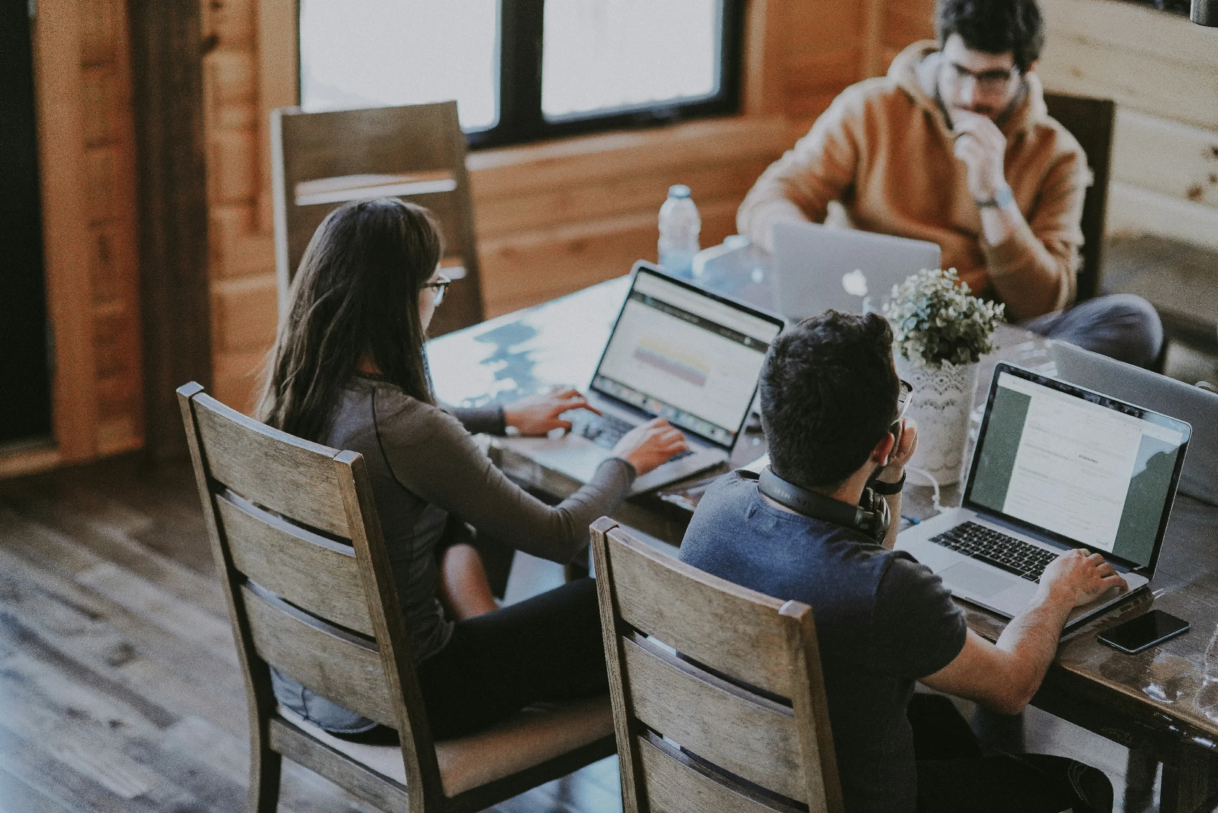 Casual modern office with 3 people working from a large table on laptops.