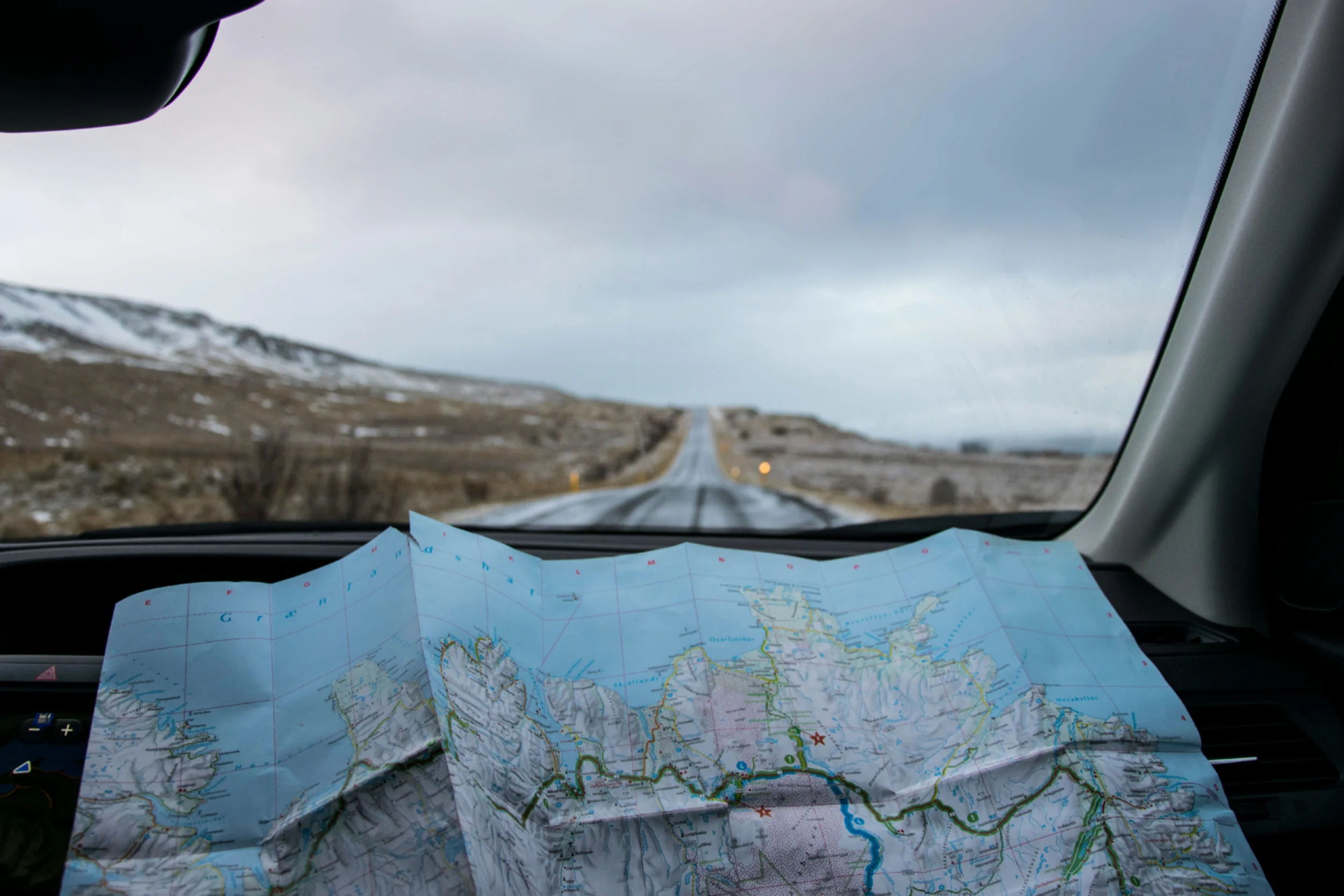 An open road map resting on the dash of car that is driving down a remote road.