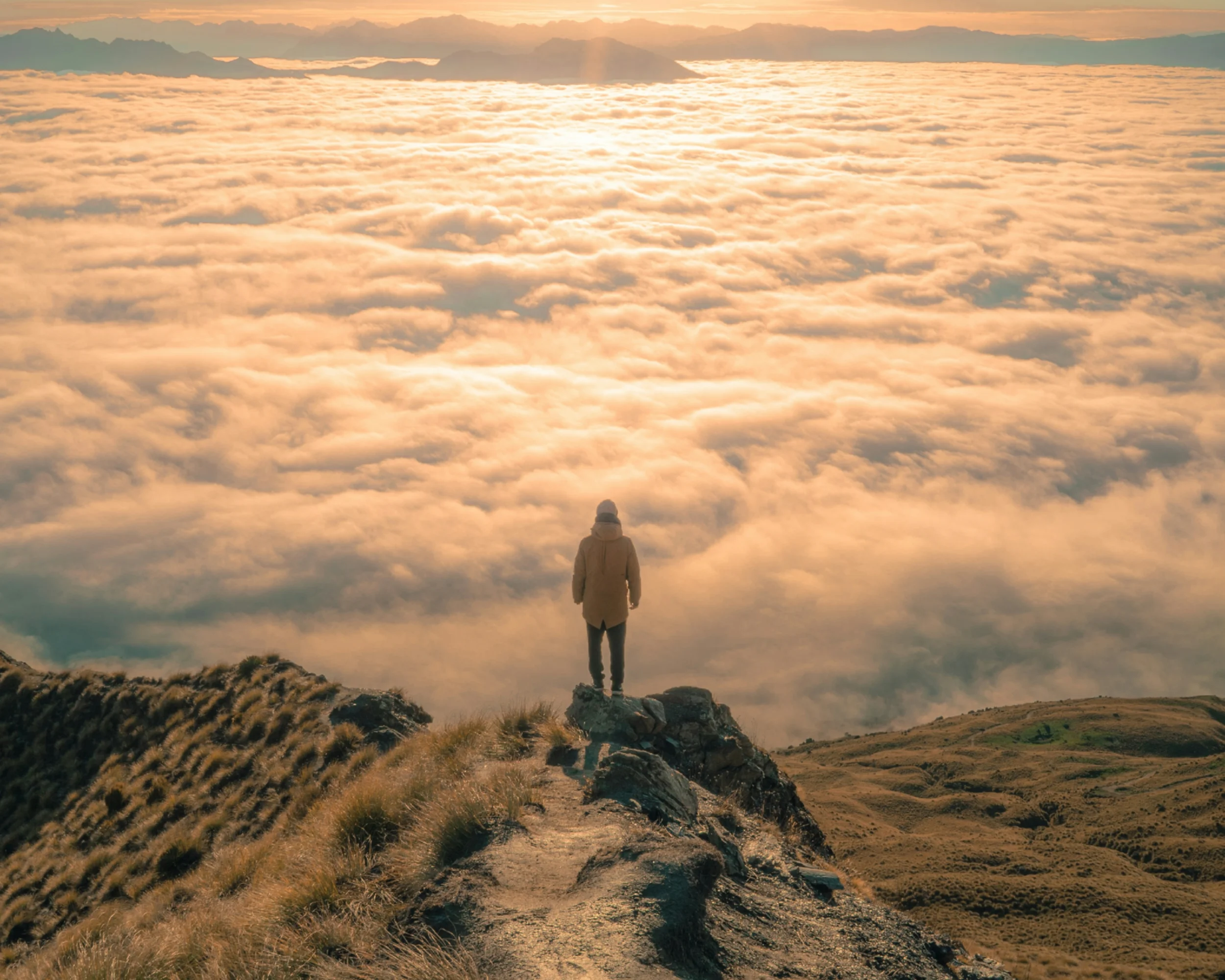 Person standing on a mountain looking out over a sea of clouds below them