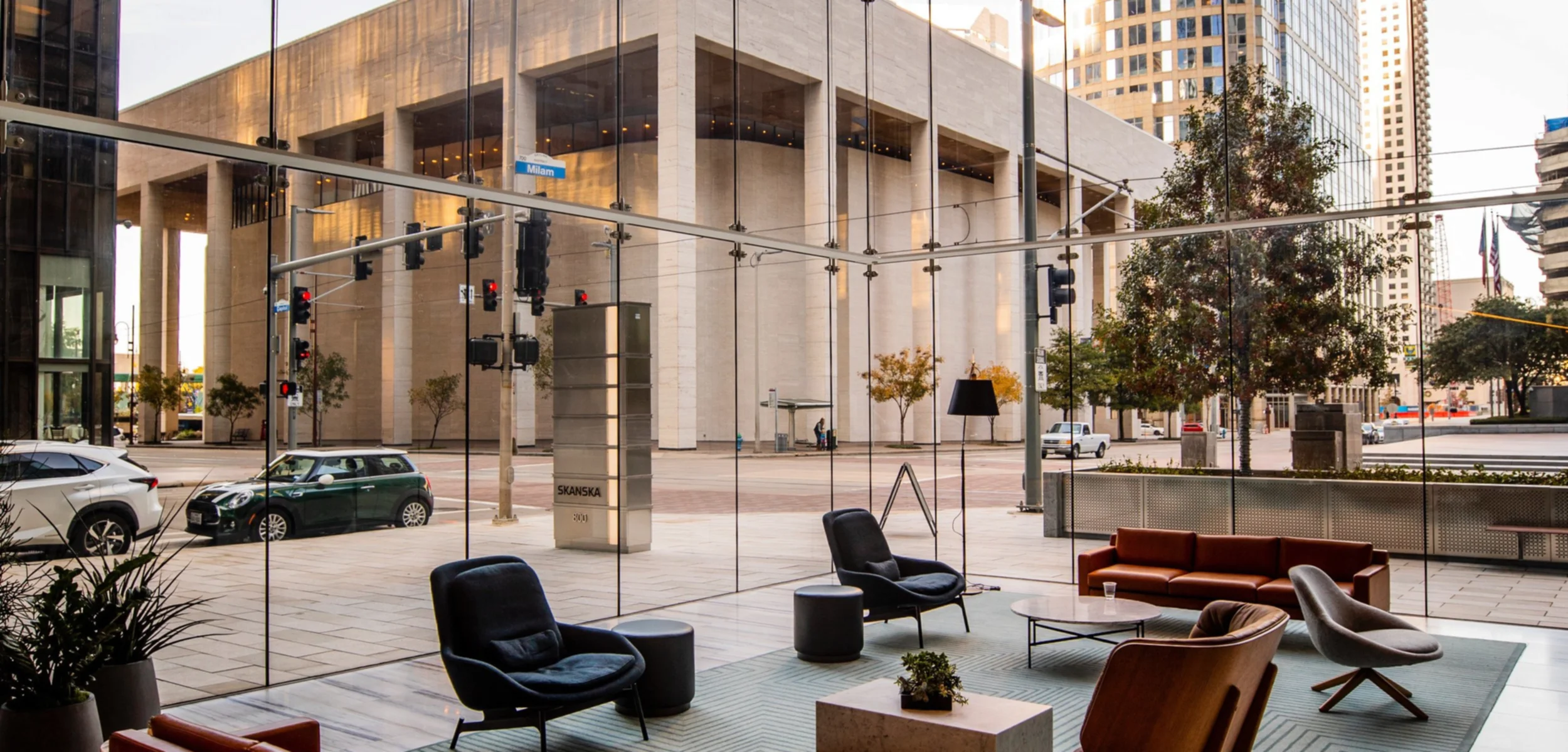 A modern and posh hotel lobby, with large glass windows allowing a view of an impressive building across the street