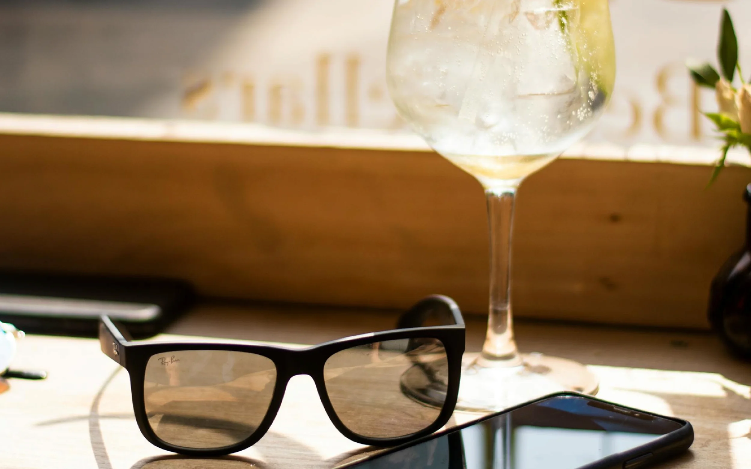 A pair of sunglasses, a phone, and a cocktail in a glass sitting on a bar