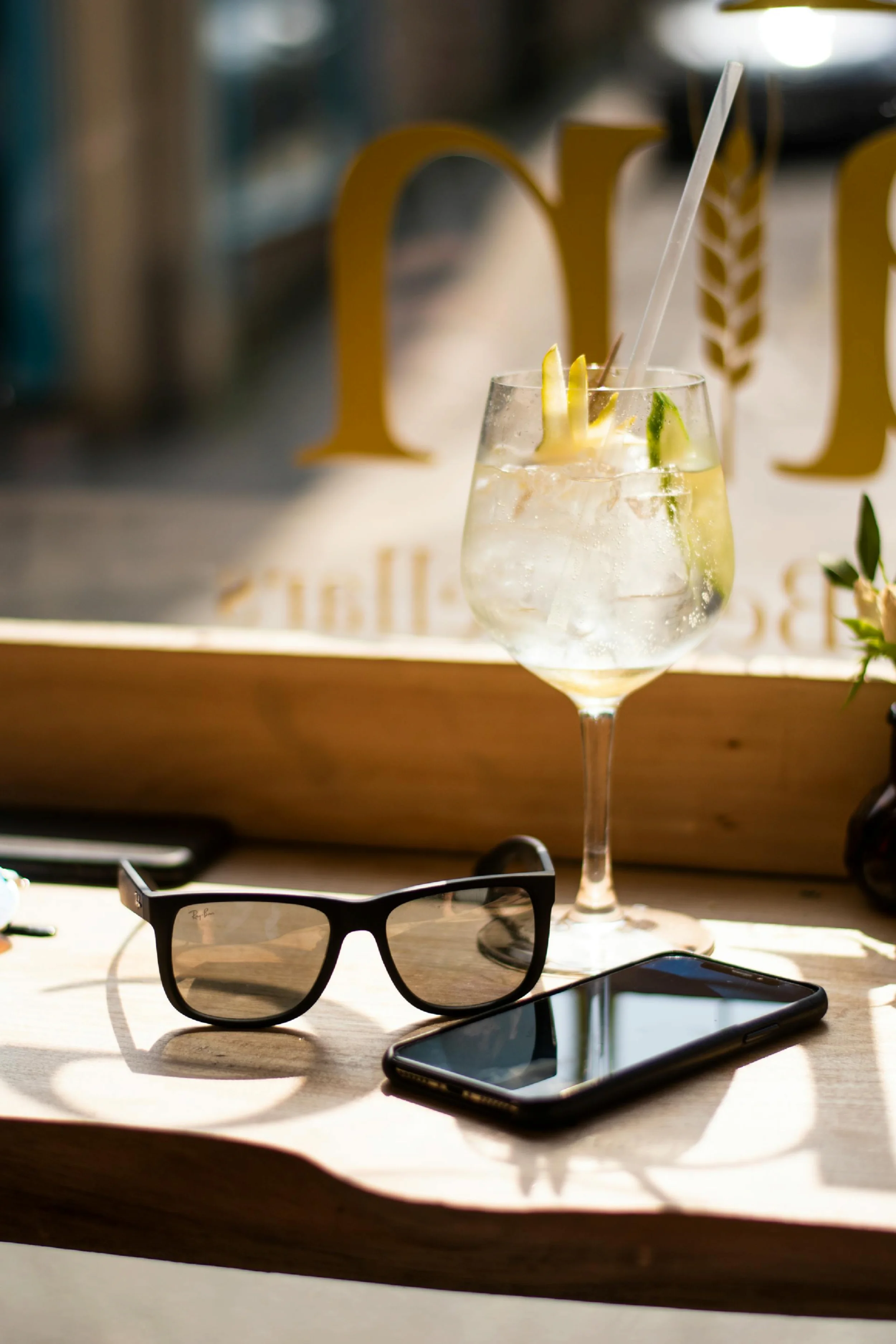A pair of sunglasses, a phone, and a cocktail in a glass sitting on a bar