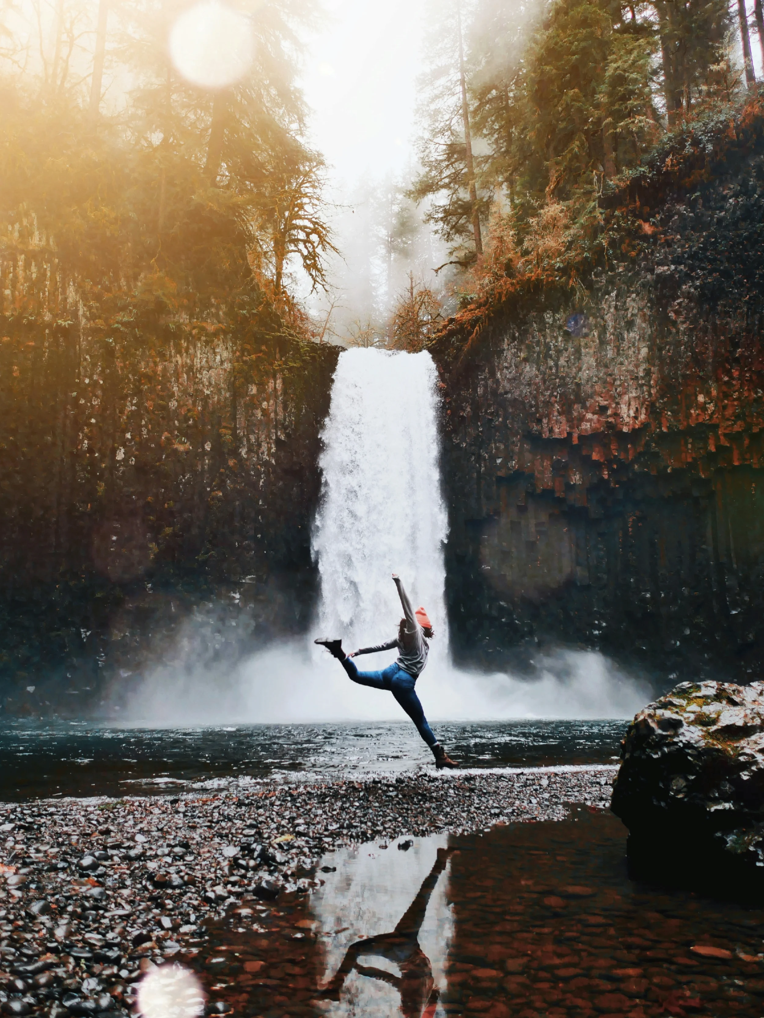 Woman leaping in front of a waterfall.