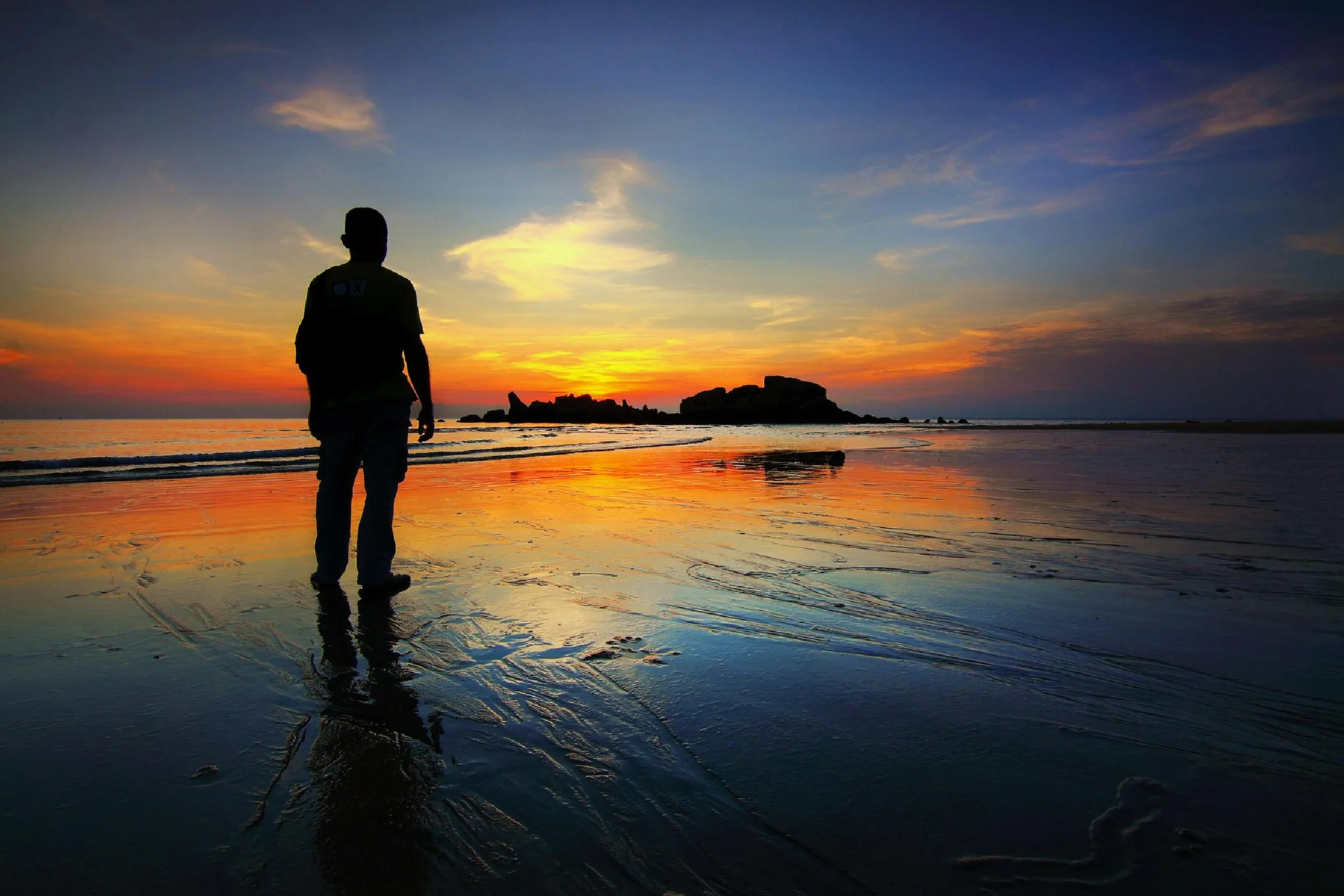 Man standing watching the sunrise on wet sand near the shore line