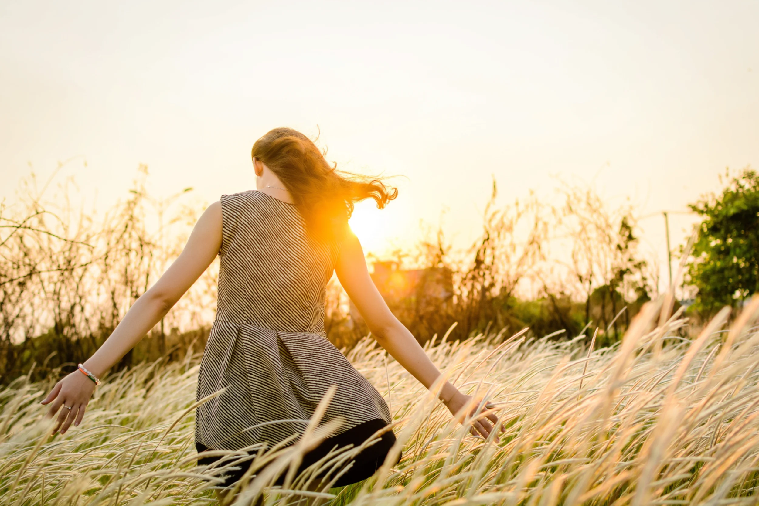 Woman walking through a field of grass with her hands outstretched