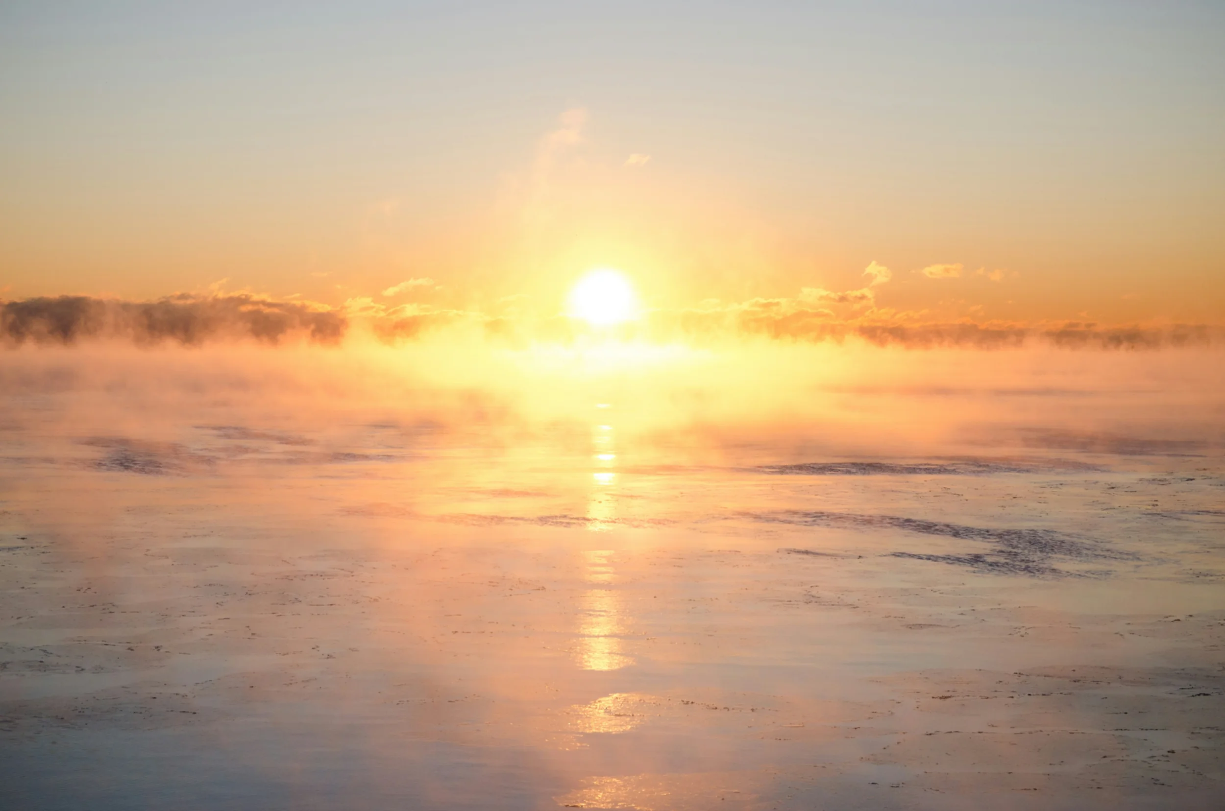 Woman standing on a rocky beach facing the sea with her arms outstretched.