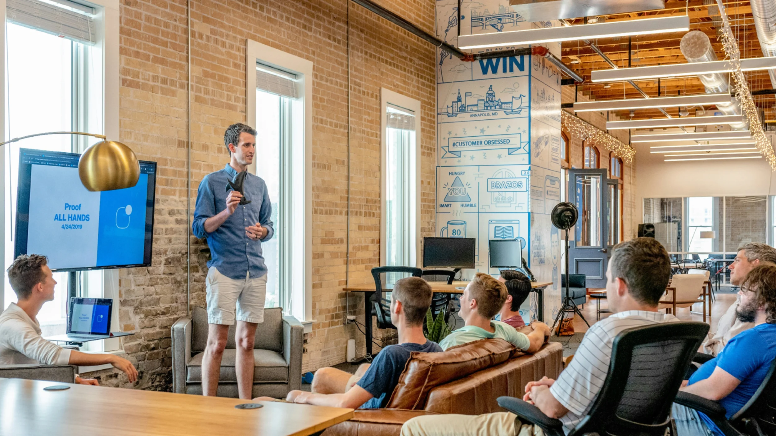A man standing in front of several people sitting on a sofa and comfortable chairs delivering a talk.