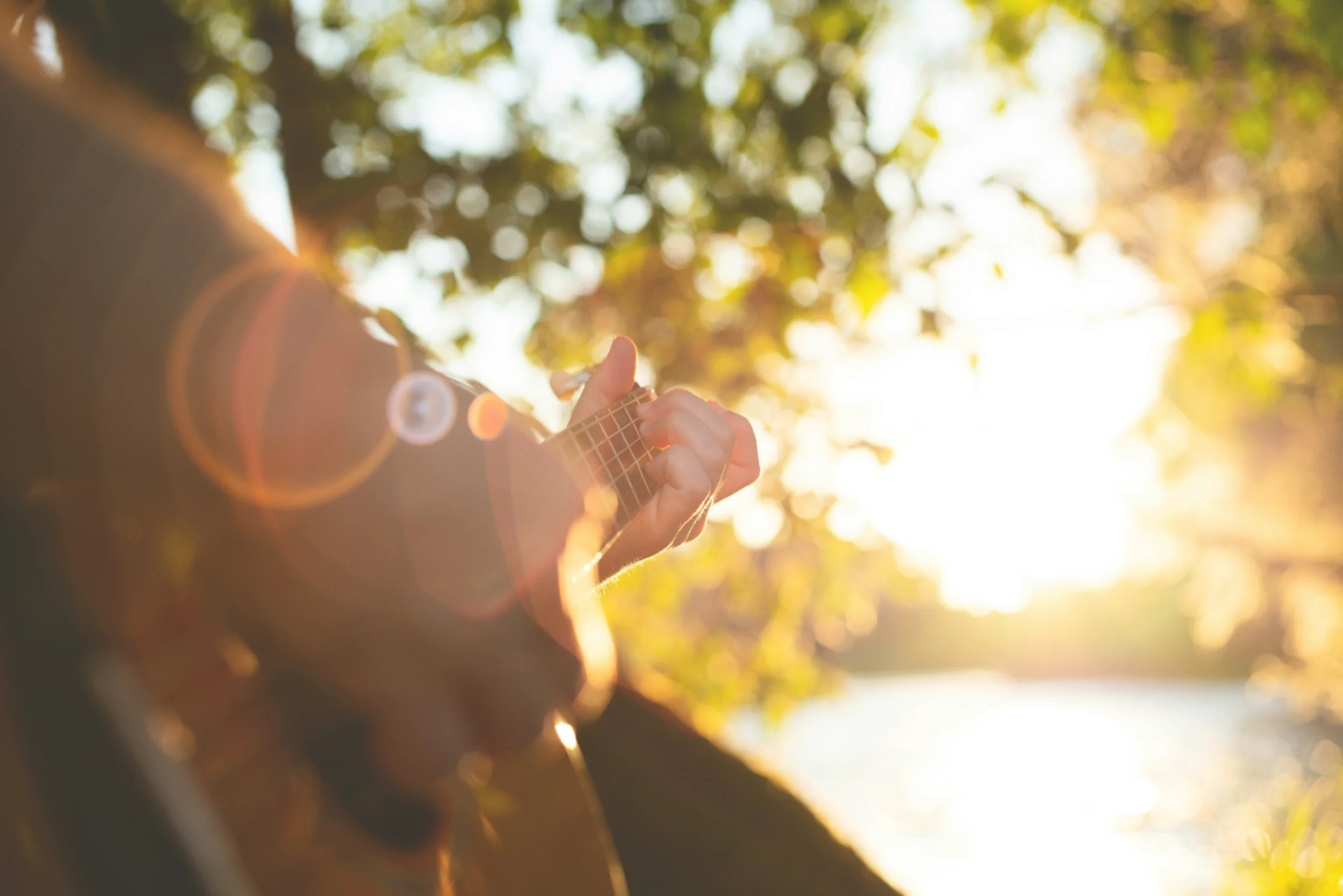 A close-up shot of a man playing a guitar outdoors on a sunny day.